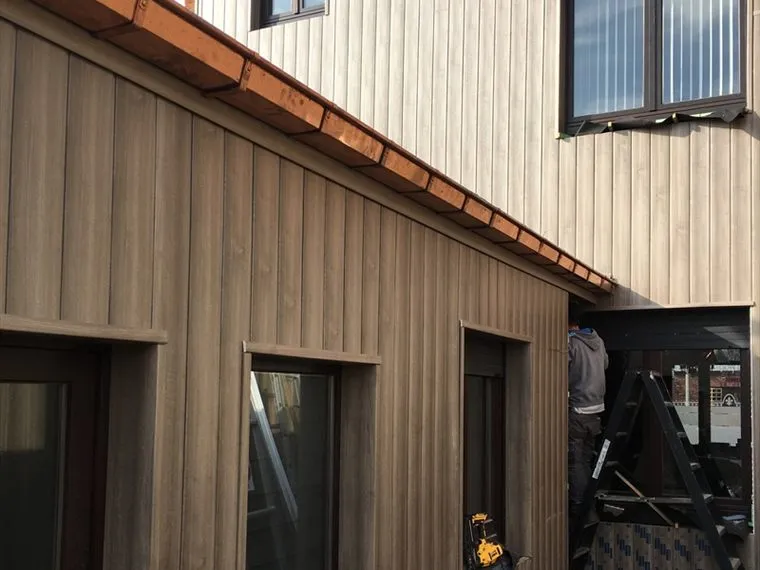 Koperen dakgoot langs een dakrand met houten gevelbekleding